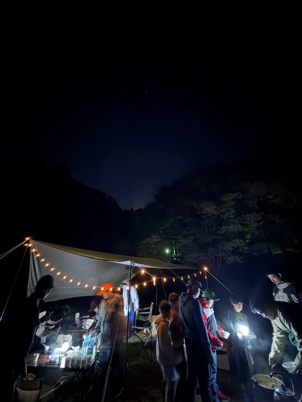夜のキャンプ場、灯りの下に集まる子どもたちとスタッフ